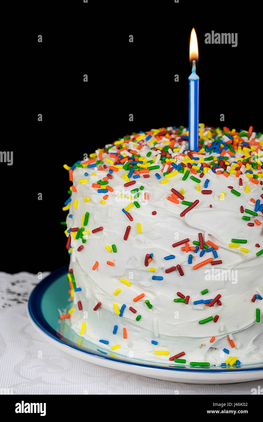 lit birthday candle on cake with white icing and candy sprinkles Stock