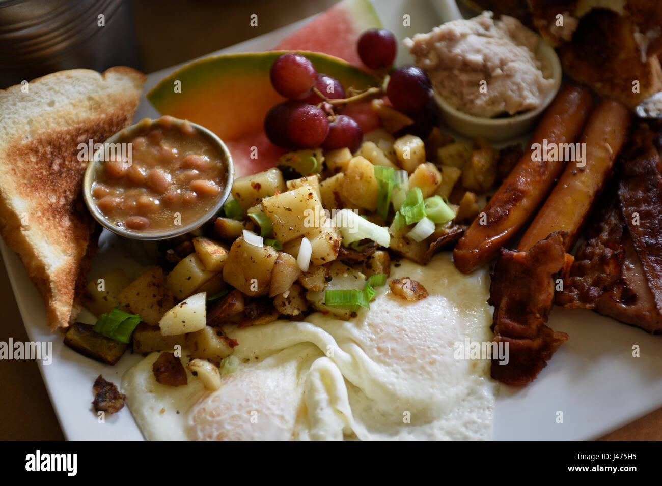 Full breakfast with french toast, fried potatos, sausages, bacon, eggs, greaves, beans an fruits Stock Photo