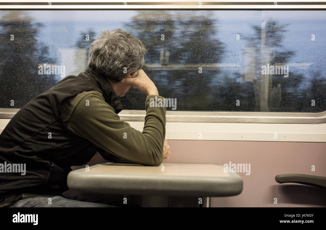 Middle aged man looking out of train window. Rain on window. UK Stock Photo