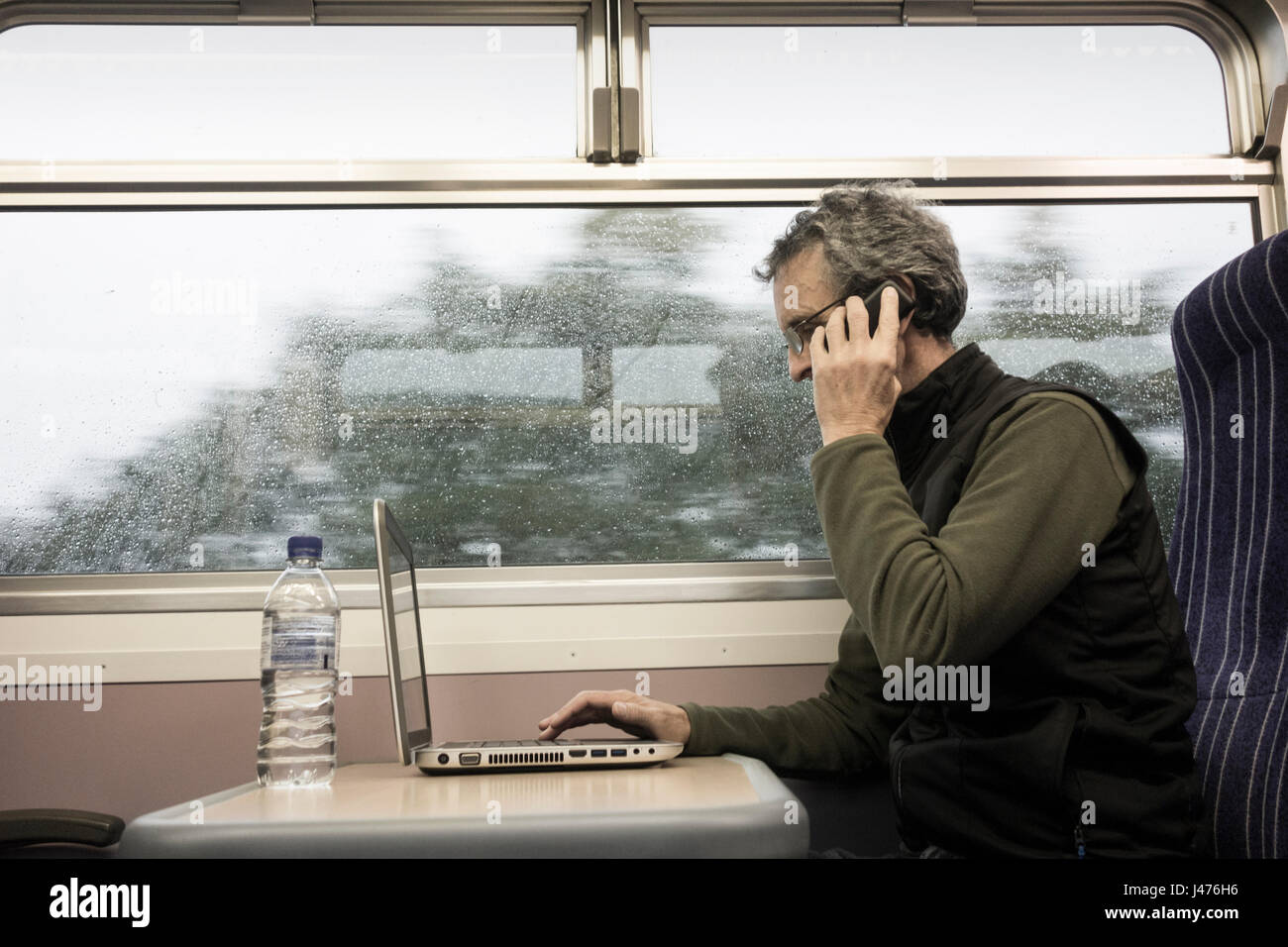 Train UK. Mature man with laptop at window seat on empty train with rain on window. England. United Kingdom Stock Photo