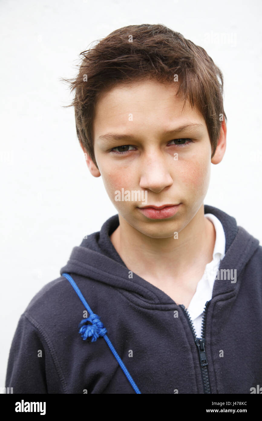 Portrait of early teenager boy looking straight at camera informal clothes brown hair white wall background Stock Photo