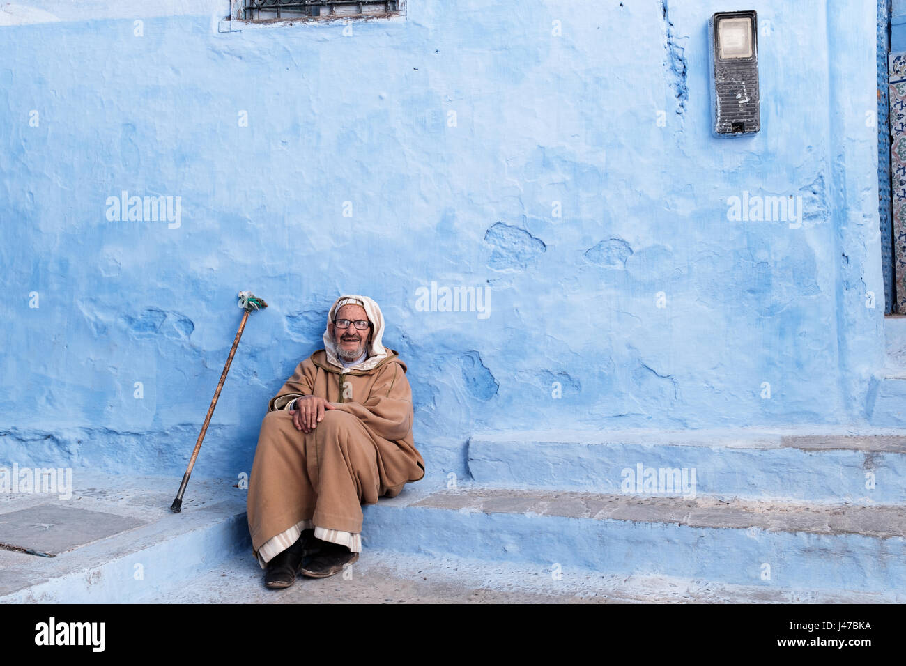 Old man resting on the street of Bright blue coloured Chefchaouen old town Stock Photo