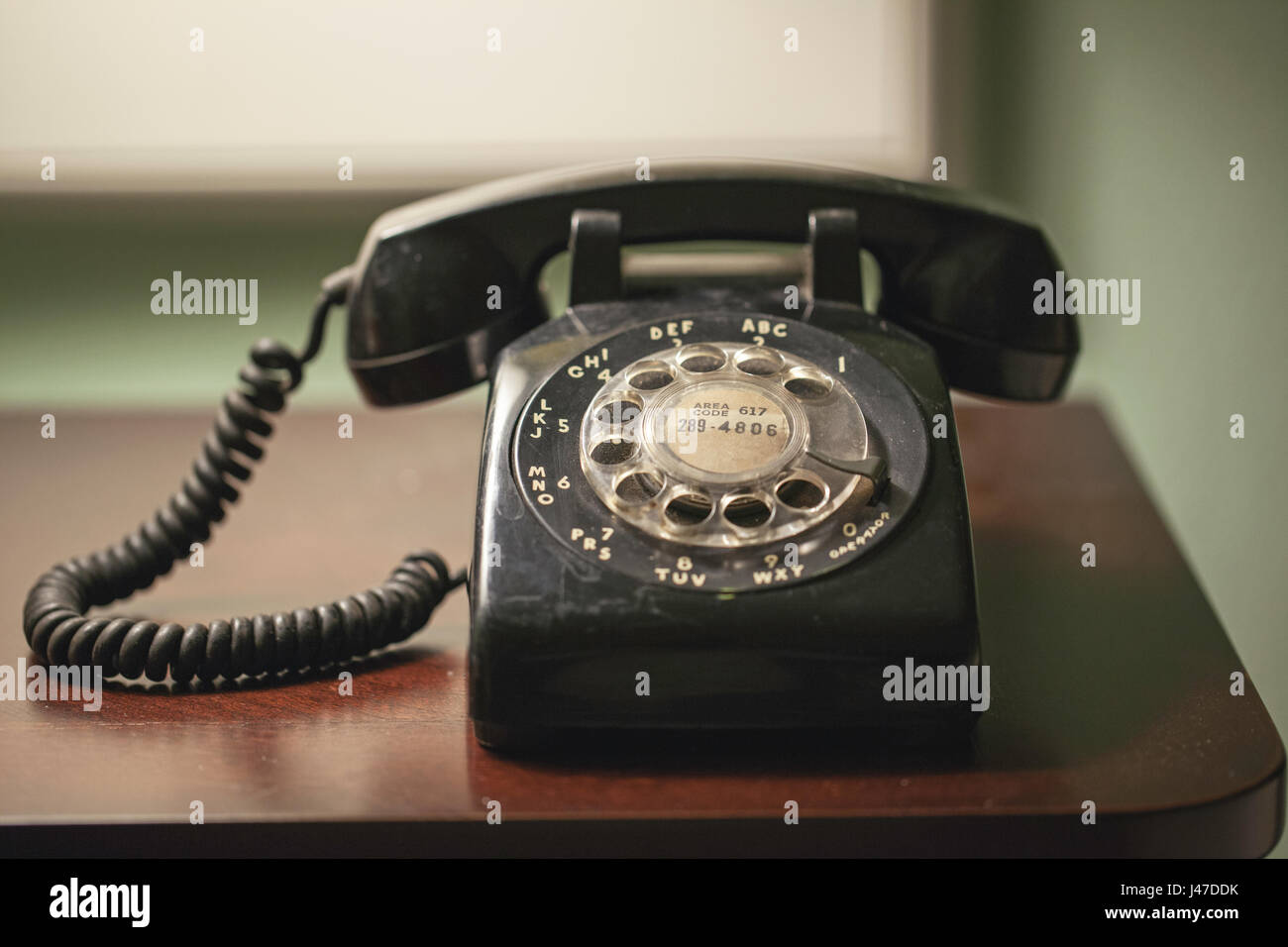 Antique retro vintage black rotary telephone wtith coiled cord on a wood desk Stock Photo