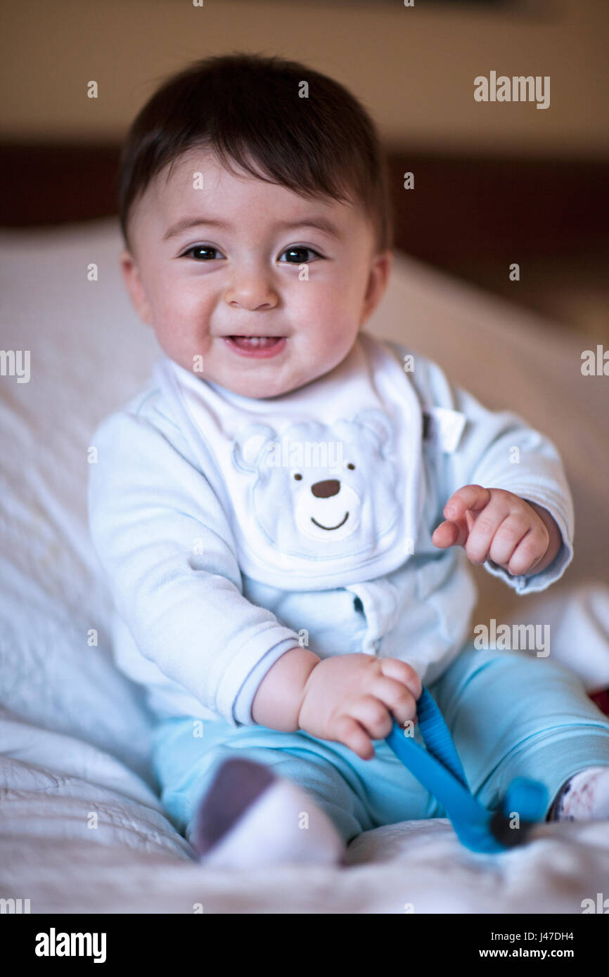 Cute smiling laughing with baby boy in blue teddy bear pajamas and bib sitting on a pillow Stock