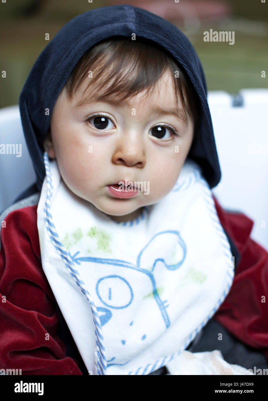 Portrait of sad serious multi-racial Asian Caucasian little boy with large brown eyes wearing a blue and maroon fleece jacket and white bib Stock Photo