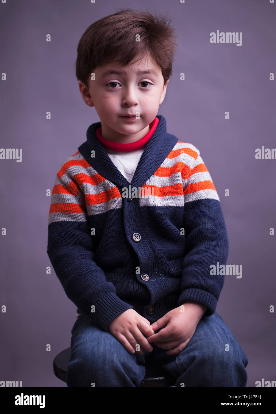 Portrait of sad serious multi-racial Asian Caucasian little boy with brown hair in a blue knitted sweater with orange strips Stock Photo