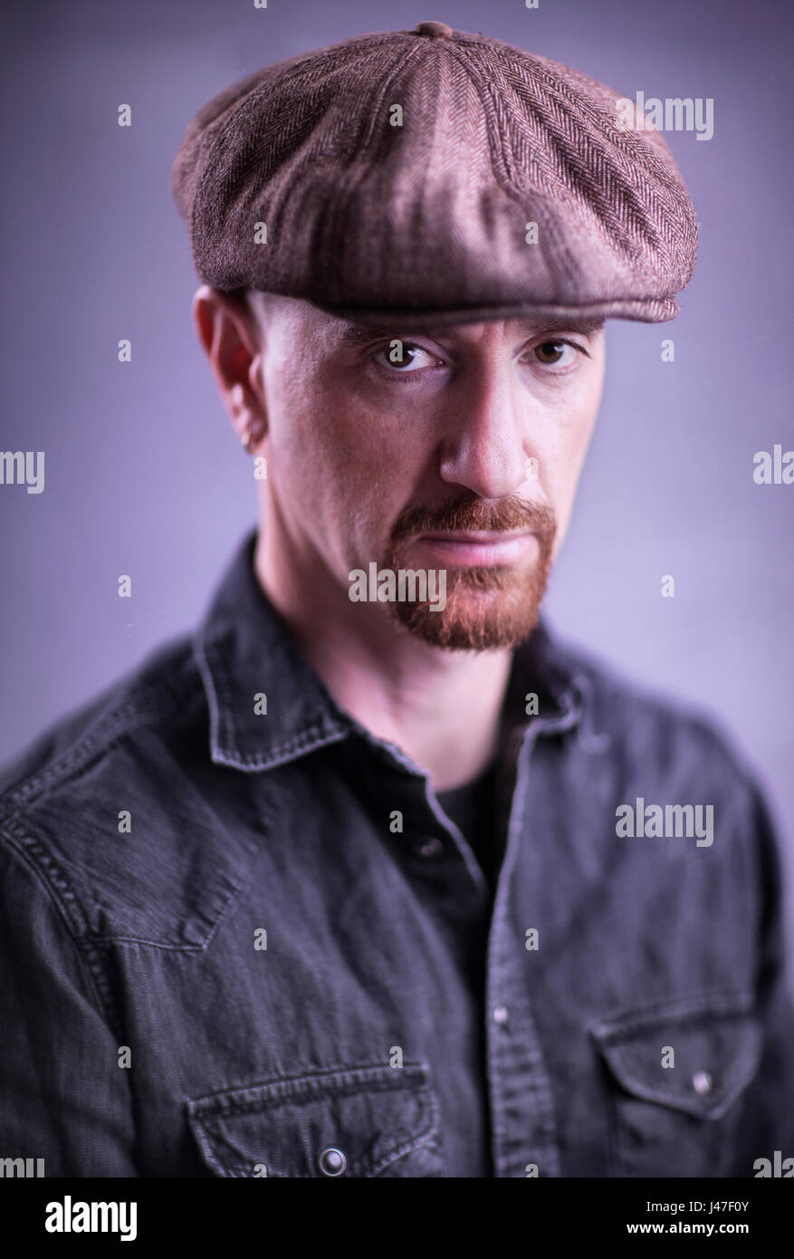 Portrait of a sad and angry man with a red goatee wearing a black denim Levis Wrangler chambray cowboy shirt and brown newsboy cap Stock Photo