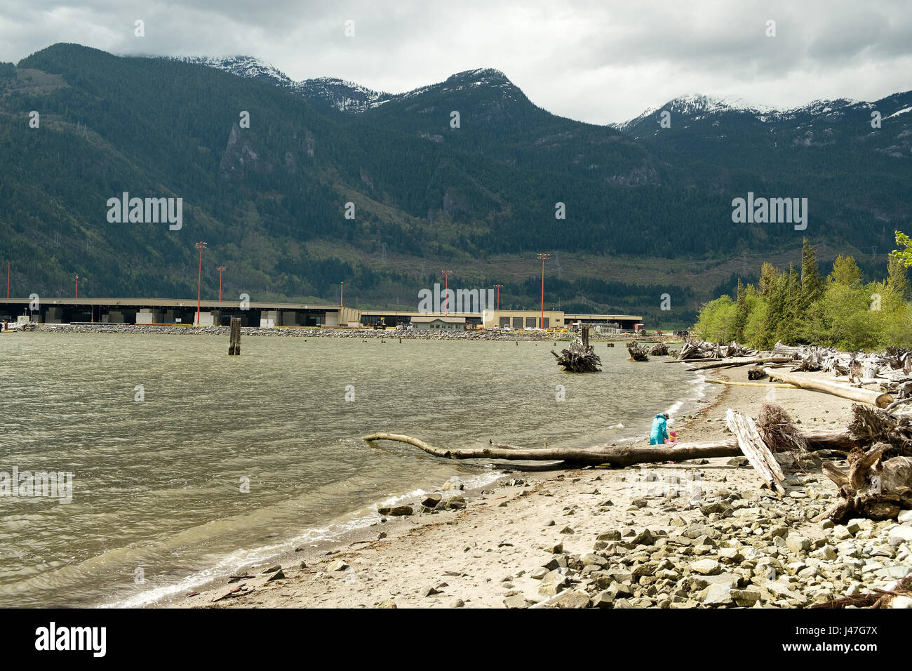 People walk along Newport Beach in Squamish BC, Canada, with the Squamish Terminal cargo port in the Background.  Squamish BC, Canada. Stock Photo