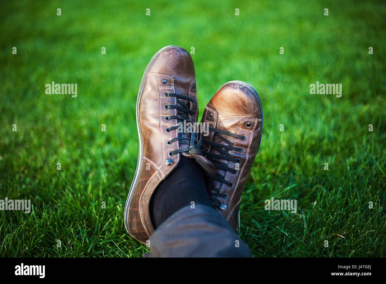 Two legs in leather shoes resting on fresh grass. Stock Photo