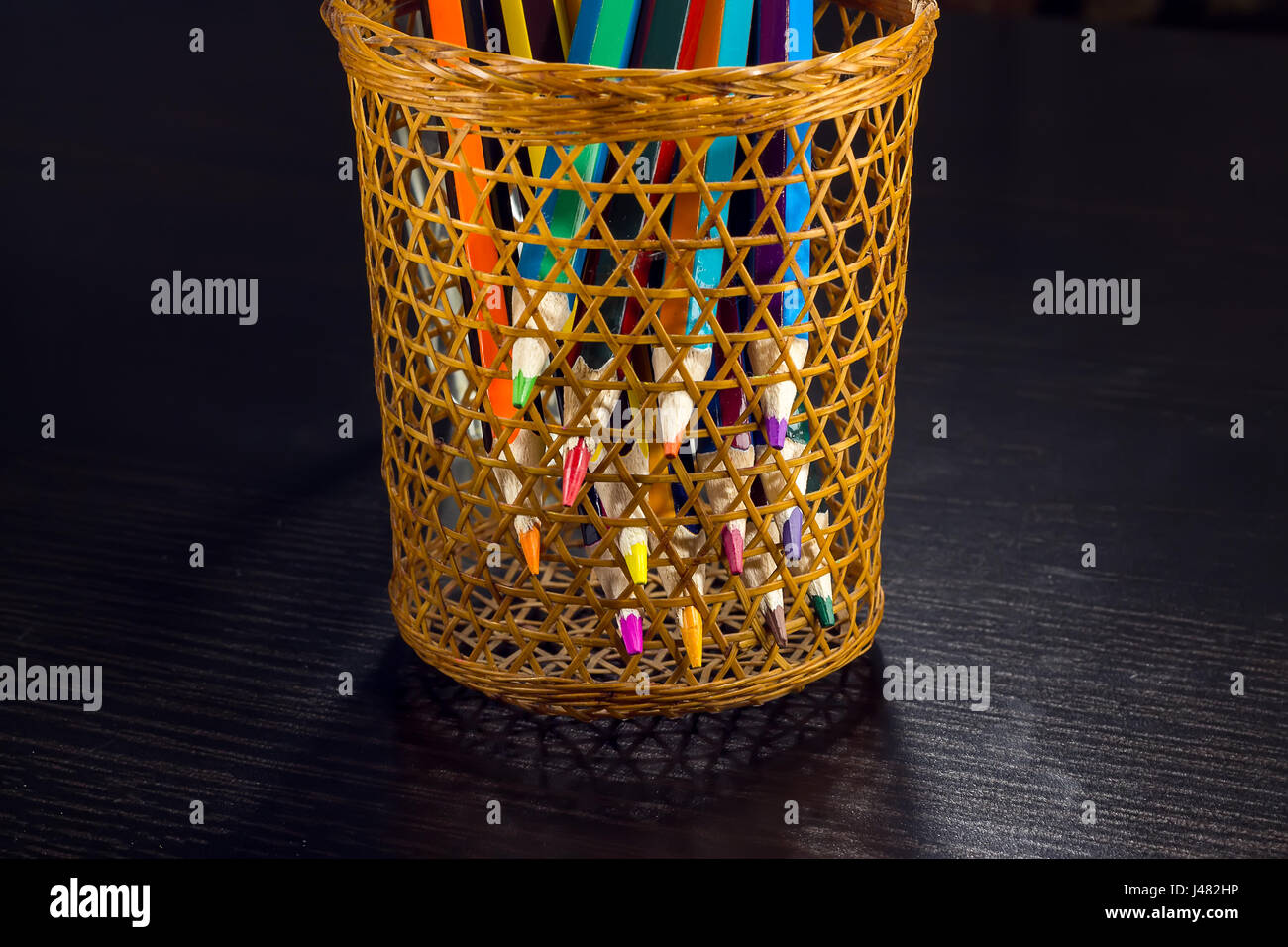 Sharp tips of colored pencils sharpen from sections of a wicker tube, on a dark wooden background Stock Photo
