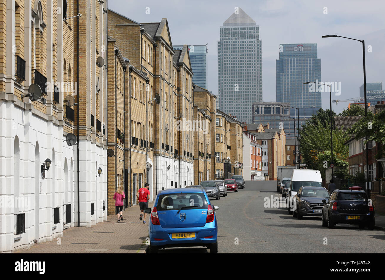 View along Rotherhithe Street in Southeast London, a residential street with the towers of Canary Wharf in the background. Shows couple jogging. Stock Photo