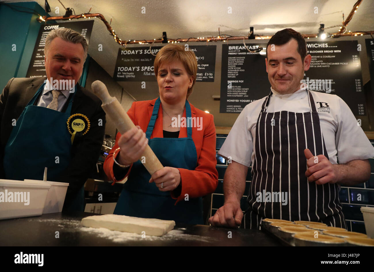 SNP Leader Nicola Sturgeon holds a rolling pin as she and the party's local candidate John Nicolson (left) make haggis pies with Table 13 Express co-owner Iain Murphy on a campaign visit to the cafe in Kirkintilloch, East Dunbartonshire. Stock Photo