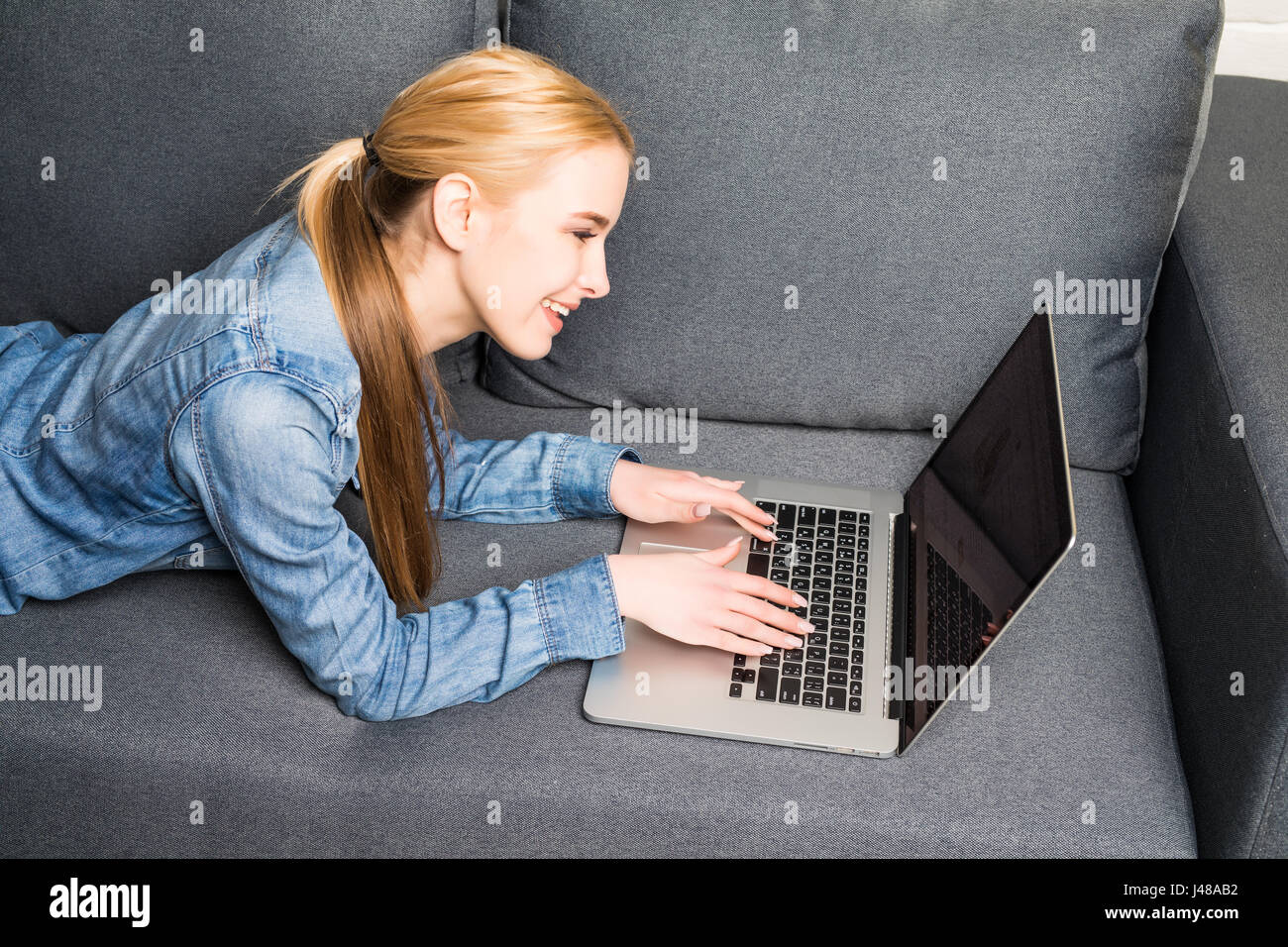 Casual young woman lying on couch and using laptop Stock Photo - Alamy