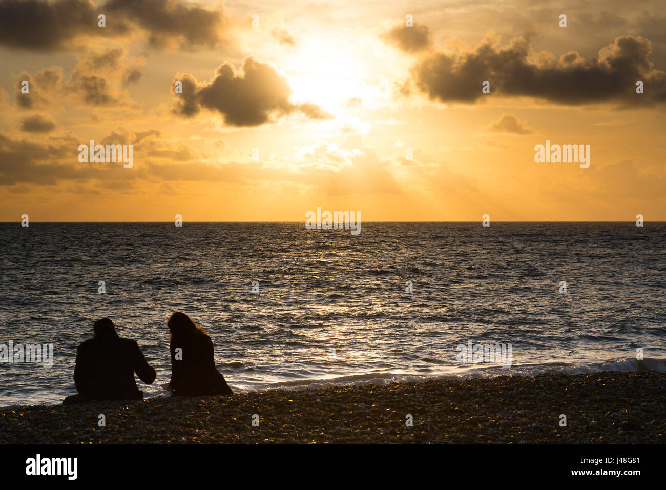 Brighton, UK. Couple sitting on shingle beach enjoying a sunset. Stock Photo
