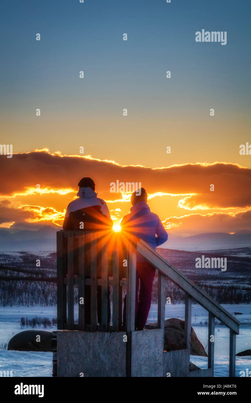 Couple enjoying a winter sunset, Lapland, Sweden Stock Photo