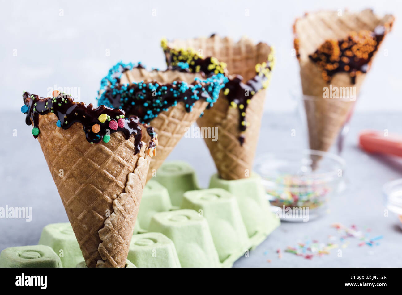 Preparing chocolate dipped ice cream cones with candy sprinkles ...