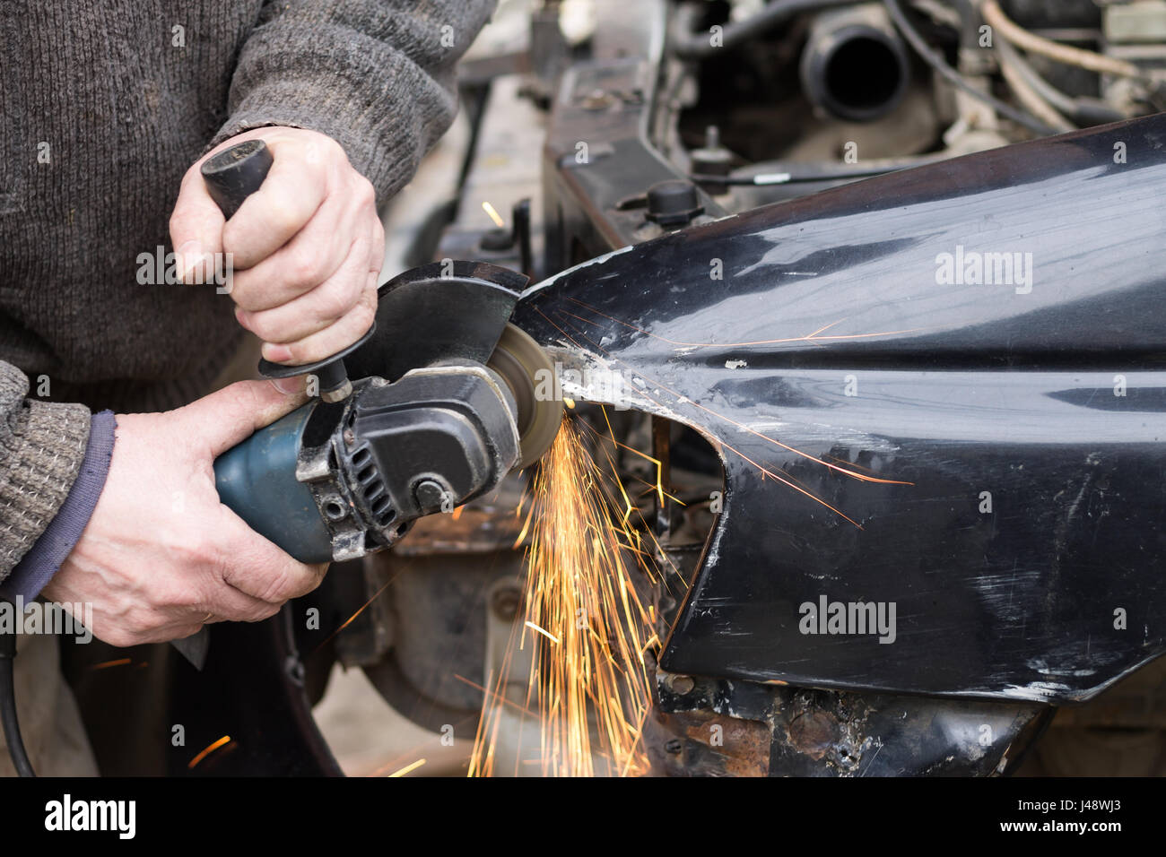 Repair service worker fix damaged car after crash on the road. Working with angle grinder to fix