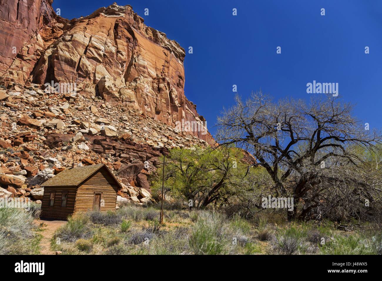 Vintage Historic Mormon Settlers Rustic Wooden Log Cabin School. Fruita, Capitol Reef National Park, with Scenic Utah Red Rock Landscape on Sunny Day Stock Photo