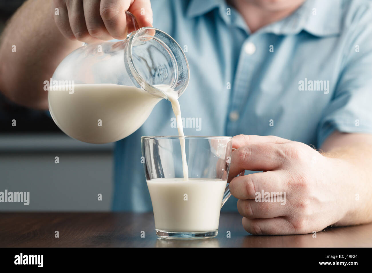 Close up of man hand pouring milk from jug to glass on a rustic wooden table  Stock Photo - Alamy