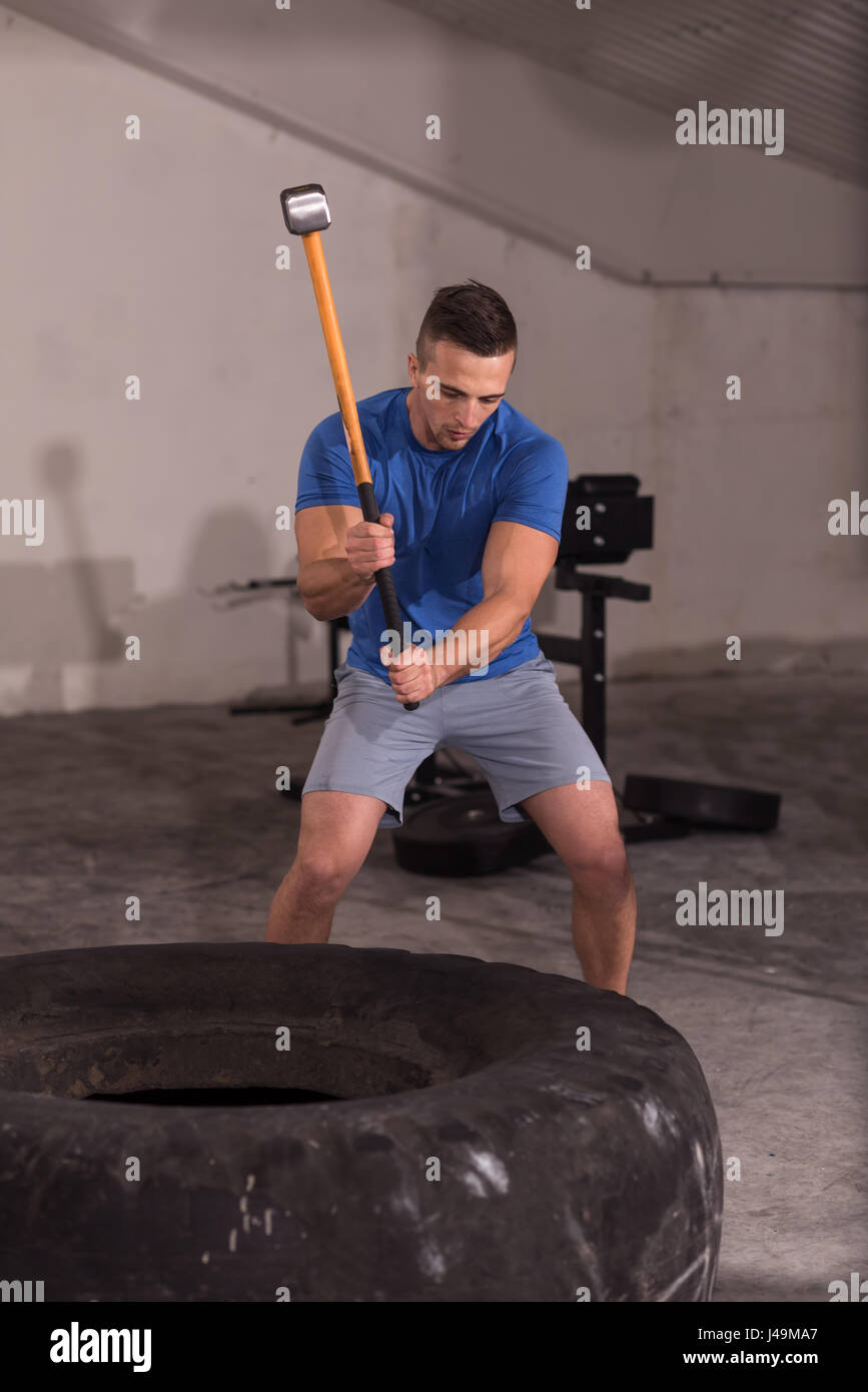 Sledgehammer Tire Hits young muscular man workout at gym with hammer