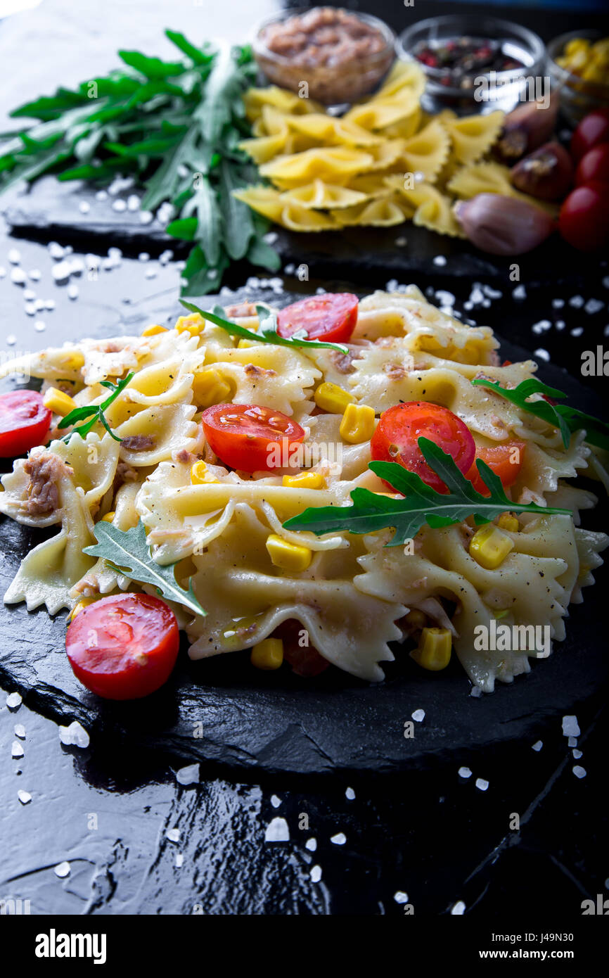 Pasta salad in slate plate with tomatoes cherry, tuna, corn and arugula