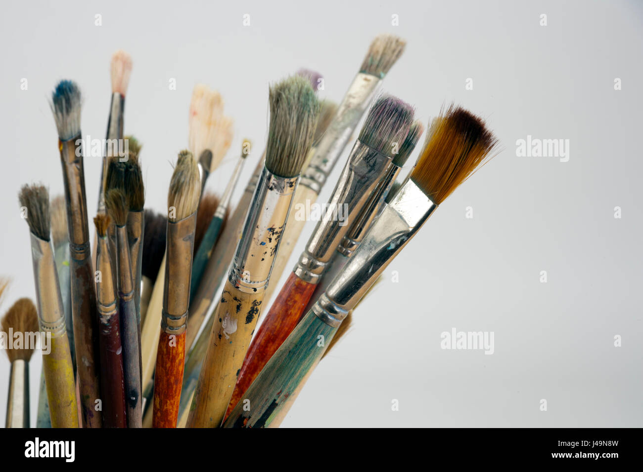 A collection of well used art paint brushes in an old jug in front of a white background Stock Photo