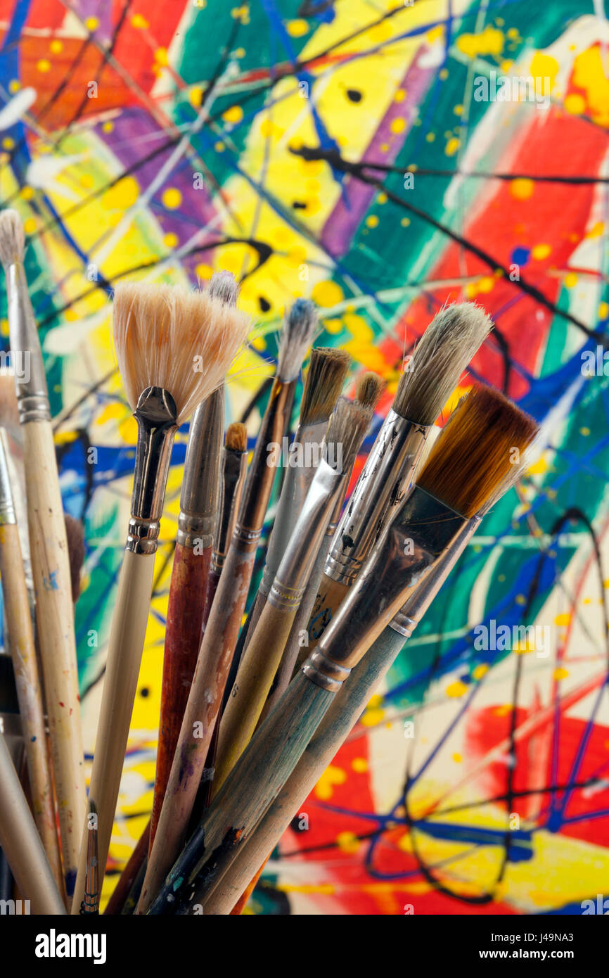 A collection of well used art paint brushes with a highly colourful abstract artwork as a background. Stock Photo