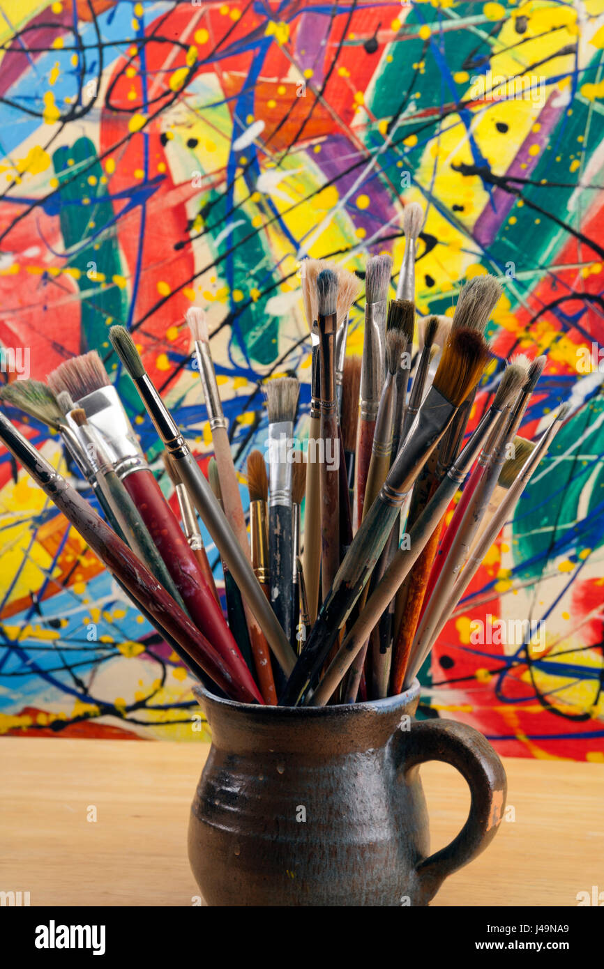A collection of well used art paint brushes with a highly colourful abstract artwork as a background. Stock Photo