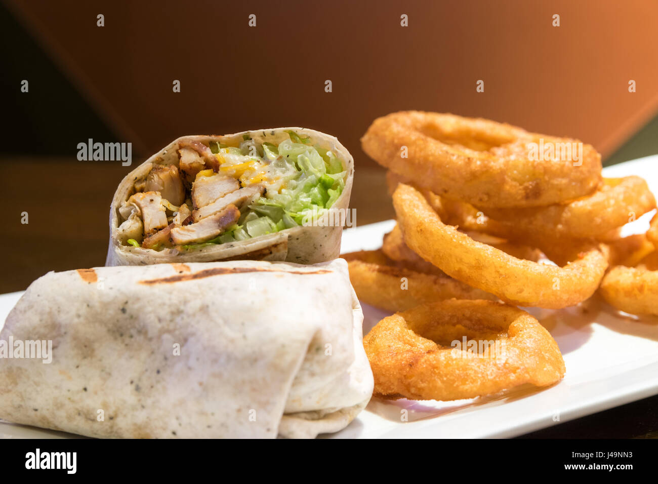 A chicken caesar wrap, served with large onion rings on a white plate. Stock Photo