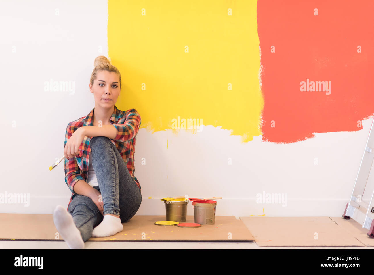 Portrait of a beautiful young female painter sitting on floor near wall ...