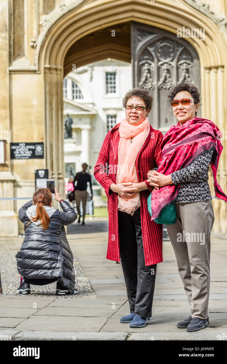 A couple of female chinese tourists pose for a photograph in front of the main entrance to King's college at the university of Cambridge, England, Bri Stock Photo