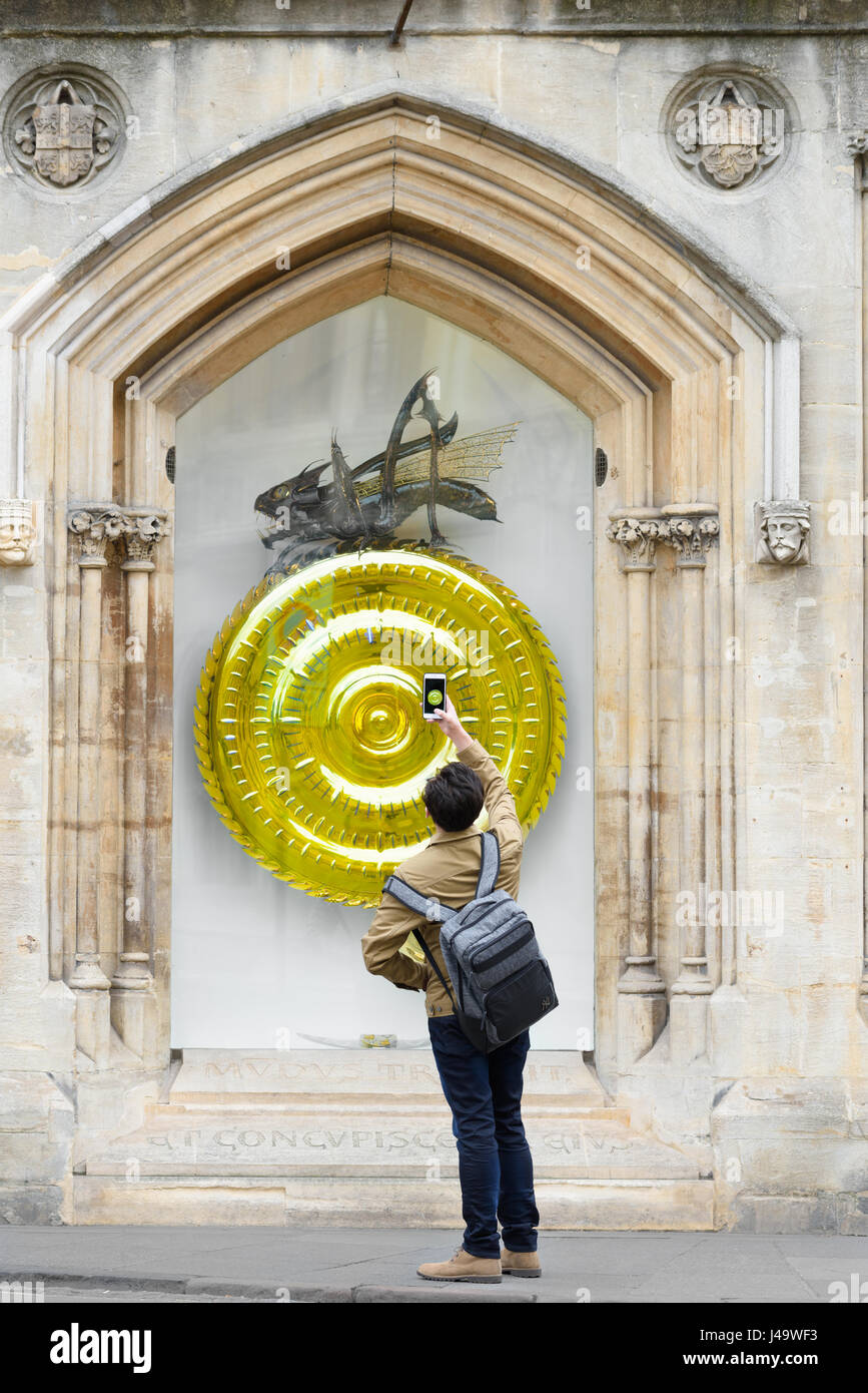 A chinese tourist uses his phone to take a photograph of the chronophage (time-eater) and large clock designed by John Taylor outside Corpus Christi c Stock Photo