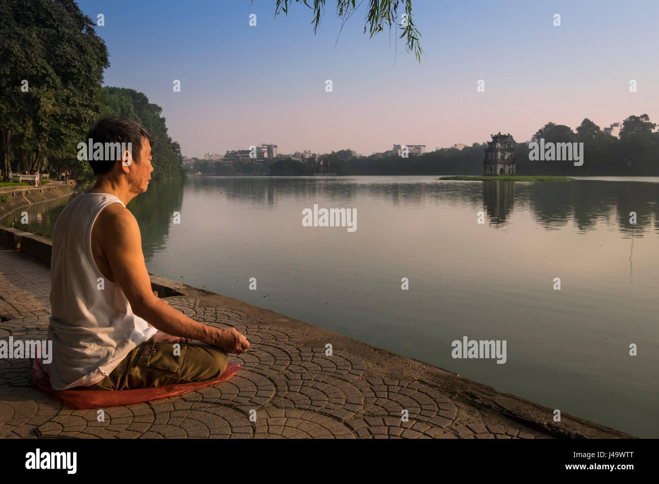 HANOI, VIETNAM - CIRCA SEPTEMBER 2014:  A Vietnamese man meditates early morning in the Hoan Kiem Lake, in Hanoi. Stock Photo