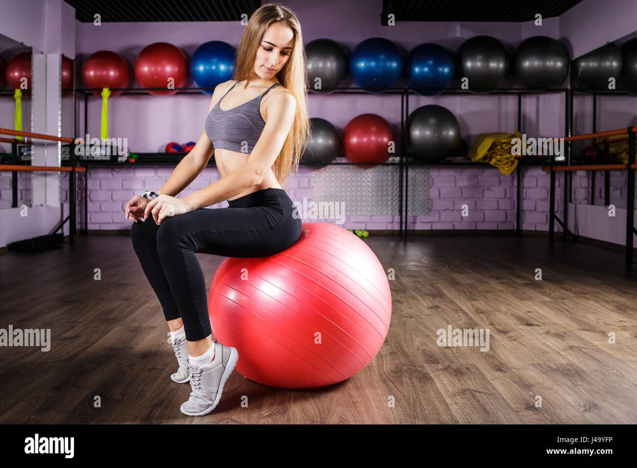 Young beautiful fitness girl sitting on fitness ball in health club
