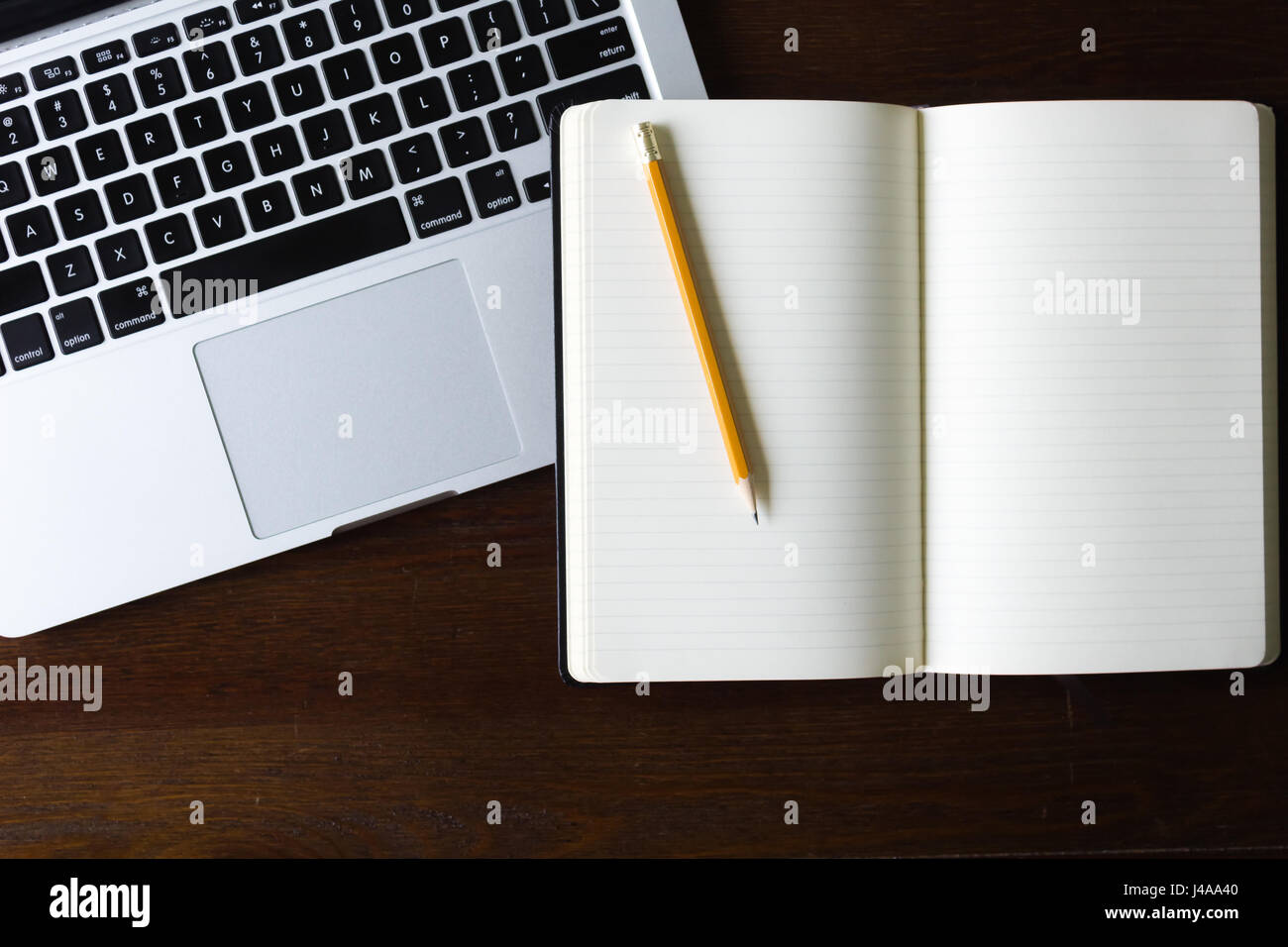 A laptop computer with a notebook and pencil on a wood table Stock Photo