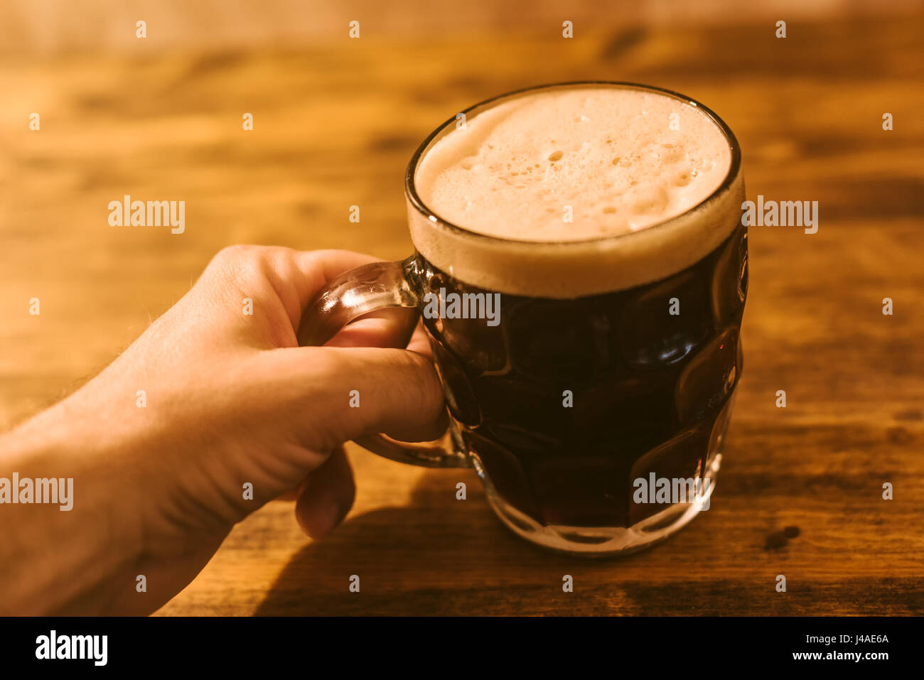 Man drinking dark beer in british dimpled glass pint mug on bar table Stock Photo