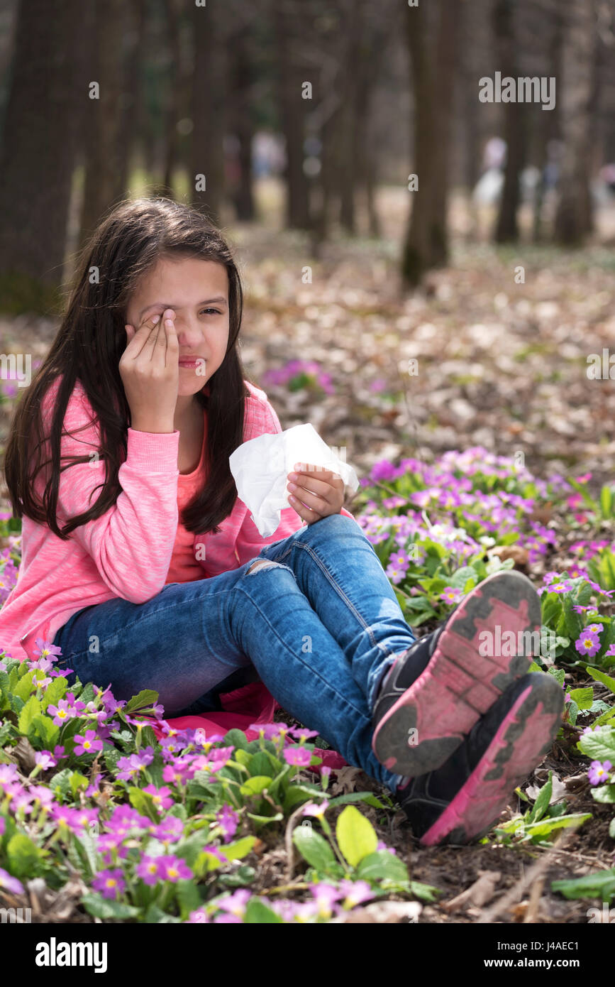 Girl holding tissue and rubbing eyes sitting on the ground Stock Photo