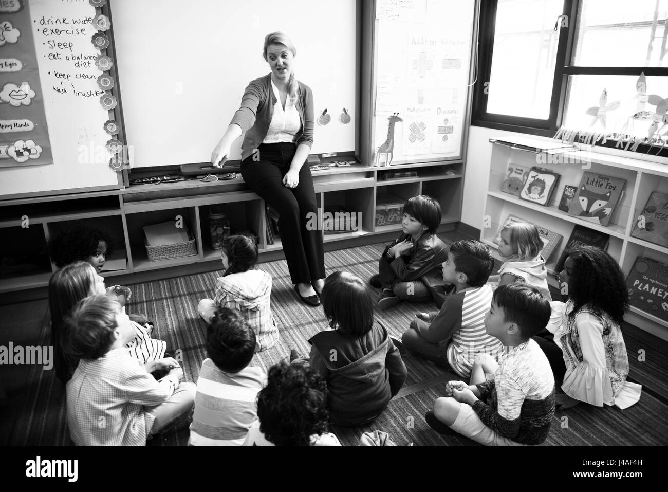 Kindergarten students sitting on the floor listening to teacher Stock Photo