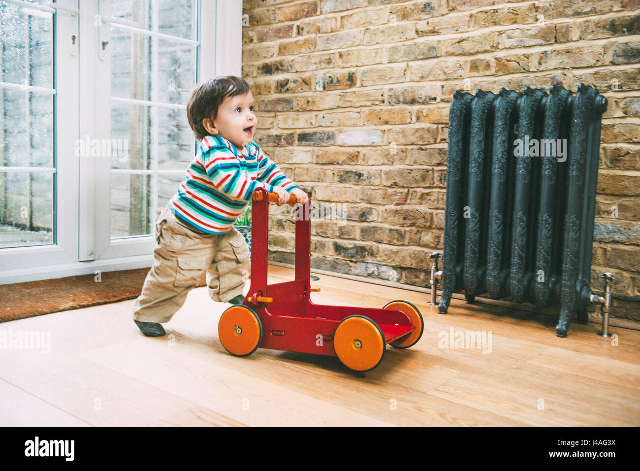 Male toddler pushing push toy on wooden floor Stock Photo