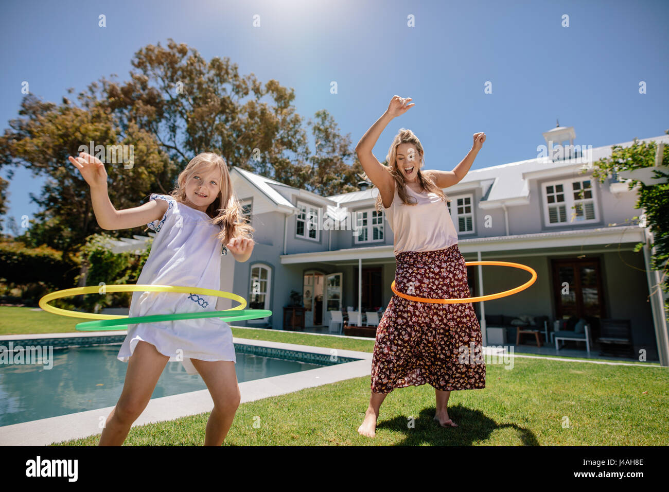 Mother and daughter playing with hula hoop in their backyard on a summer day. Happy young family having fun with hula hoop outdoors. Stock Photo