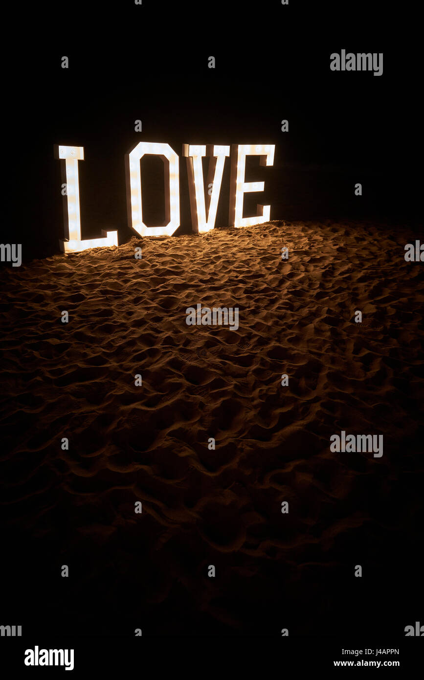 Big lighted letter in the sand on a beach at night spelling the word LOVE Stock Photo