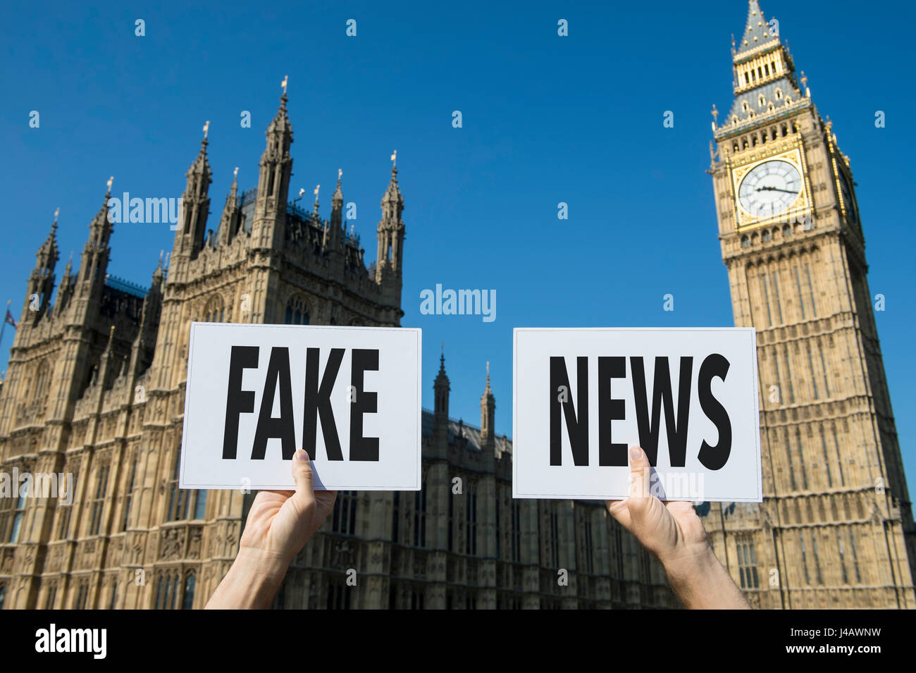 Hands holding sign protesting fake news in front of the Houses of Parliament at Westminster Palace in London, England Stock Photo