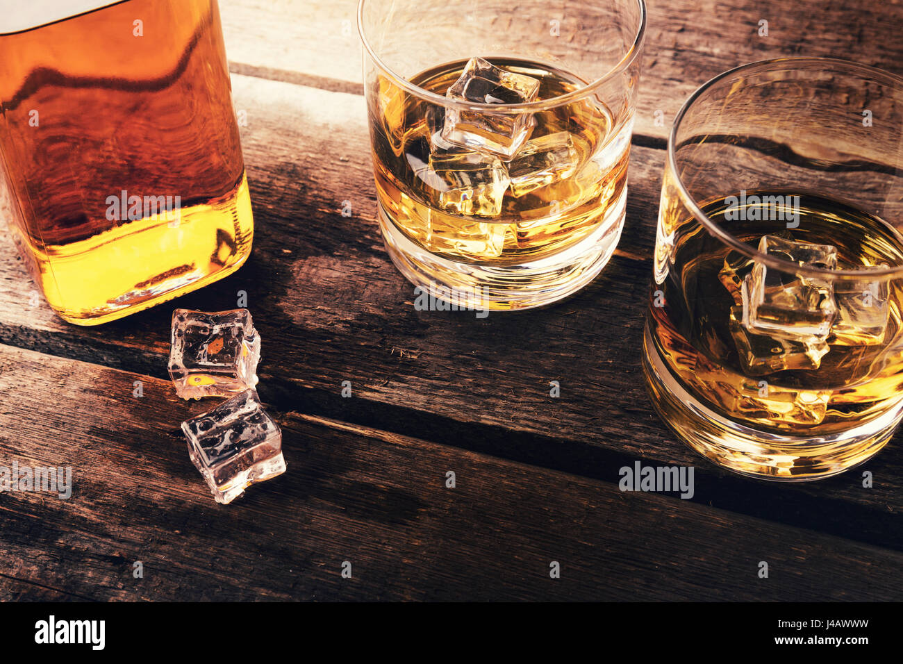 whiskey bottle and glasses with ice on dark wooden table Stock Photo