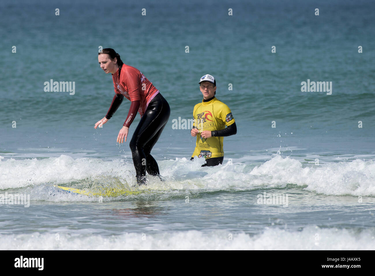 A surf school instructor teaching a novice Fistral Beach Newquay Cornwall Surfing Surfer Surf coach Learner Learning Instructor Helping Stock Photo