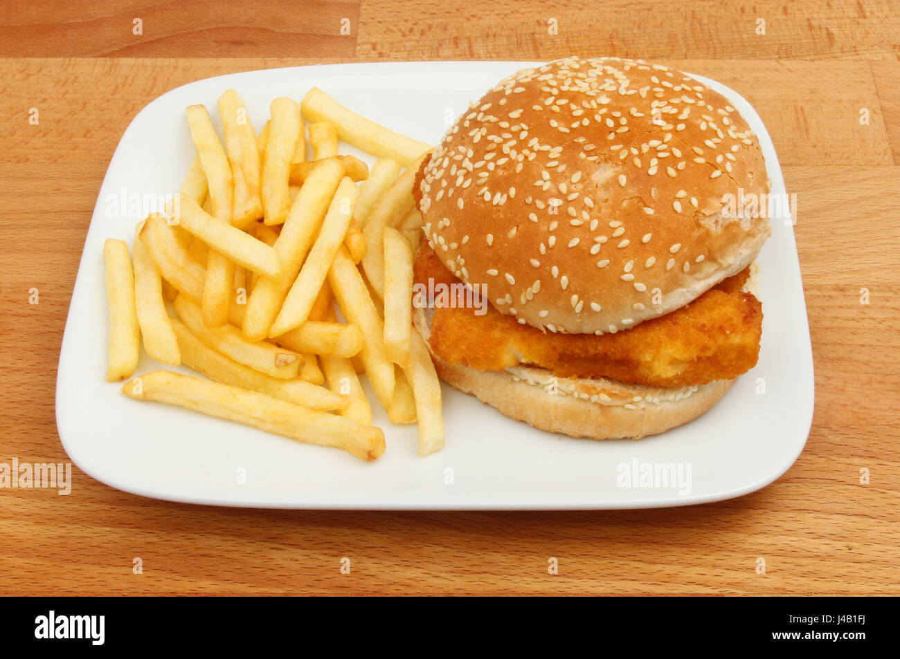 Fish burger, fish fingers in a burger bun with French fries on a plate on a wooden tabletop Stock Photo