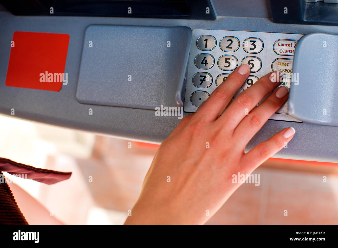 Close up of hand entering pin at an ATM. Finger about to press a pin code on a pad. Security code on an Automated Teller Machine. Female arms, ATM - e Stock Photo