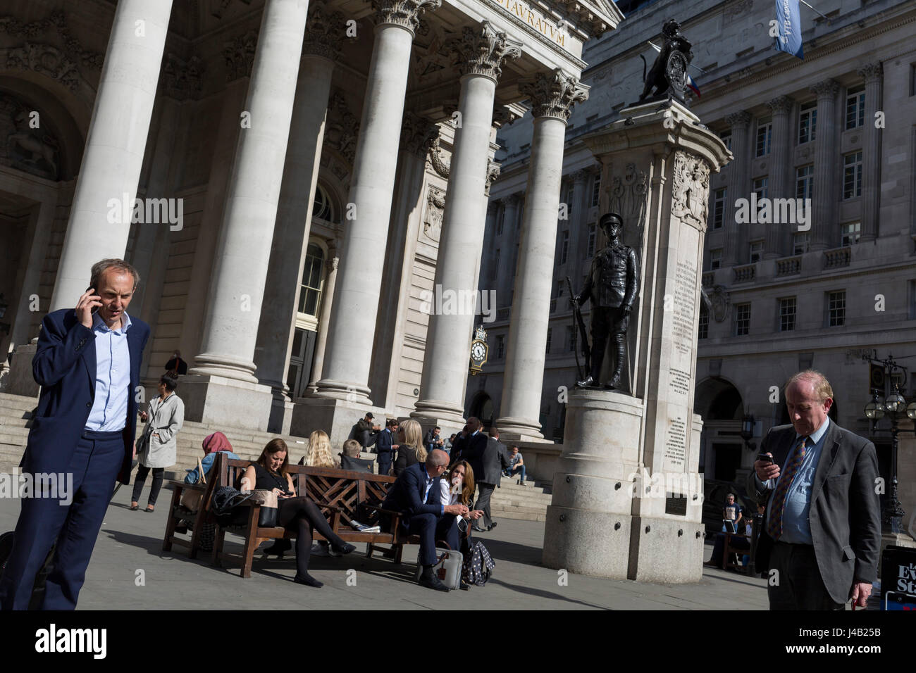 Businessmen check messages below the classical architecture of Royal Exchange and the WW1 war memorial at Bank Triangle, on 10th May 2017, in the City of London, England. Stock Photo