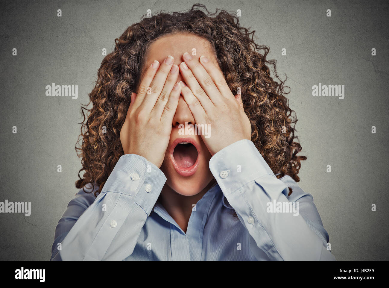 Headshot young scared woman covering eyes wide open mouth isolated on grey wall background. Human emotions face expressions feelings reaction percepti Stock Photo