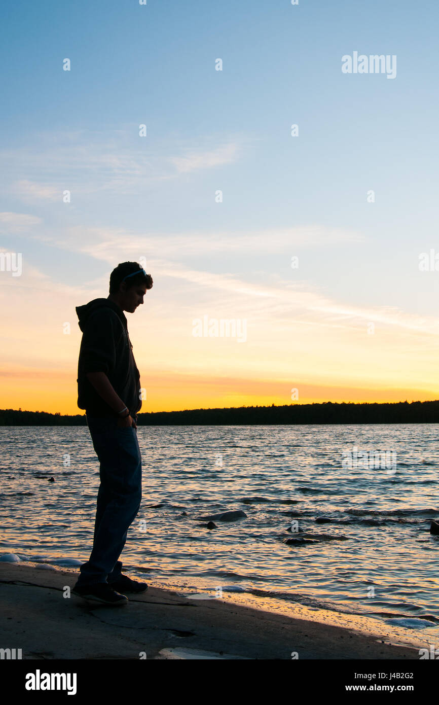 teenage boy watches the sun rise over a lake Stock Photo