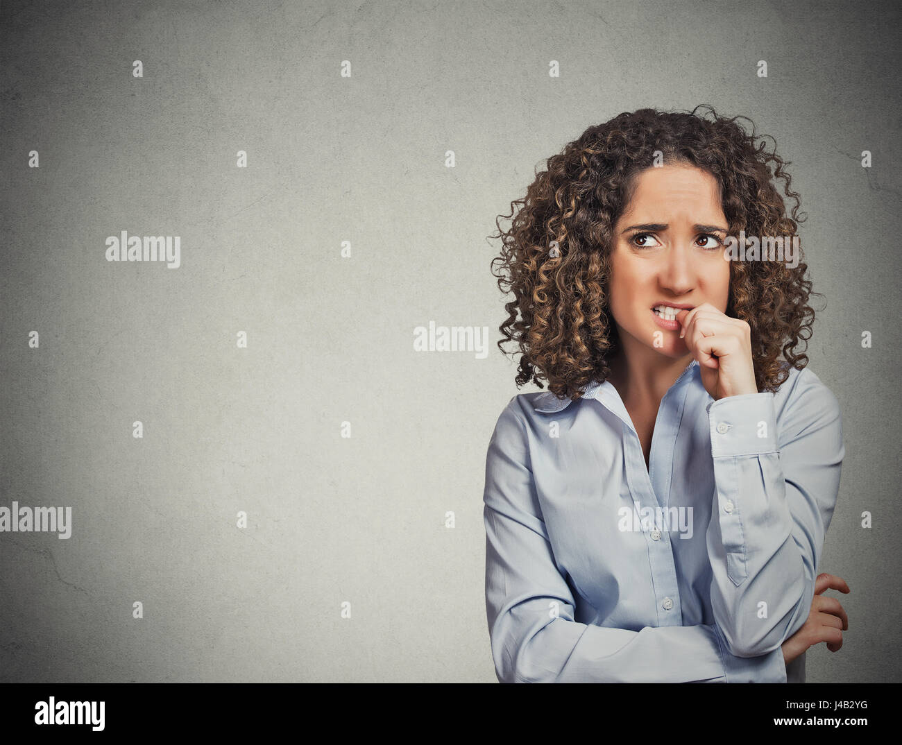 Closeup portrait nervous looking woman biting her fingernails craving something anxious isolated grey wall background with copy space. Negative human  Stock Photo